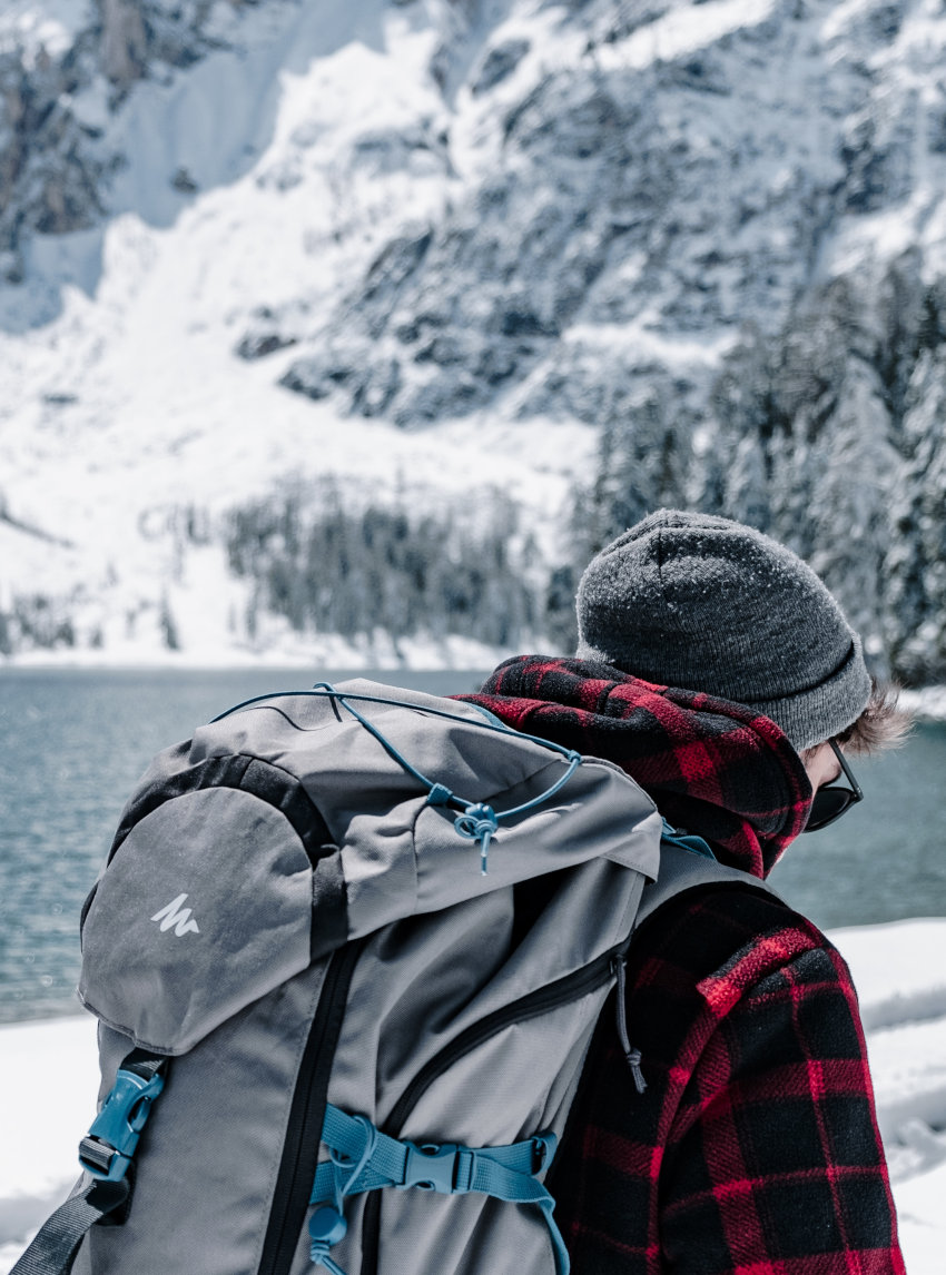 Winterlandschaft mit jungem Mann in Karohemd und einem grauen Backpacker-Rucksack auf dem Rücken